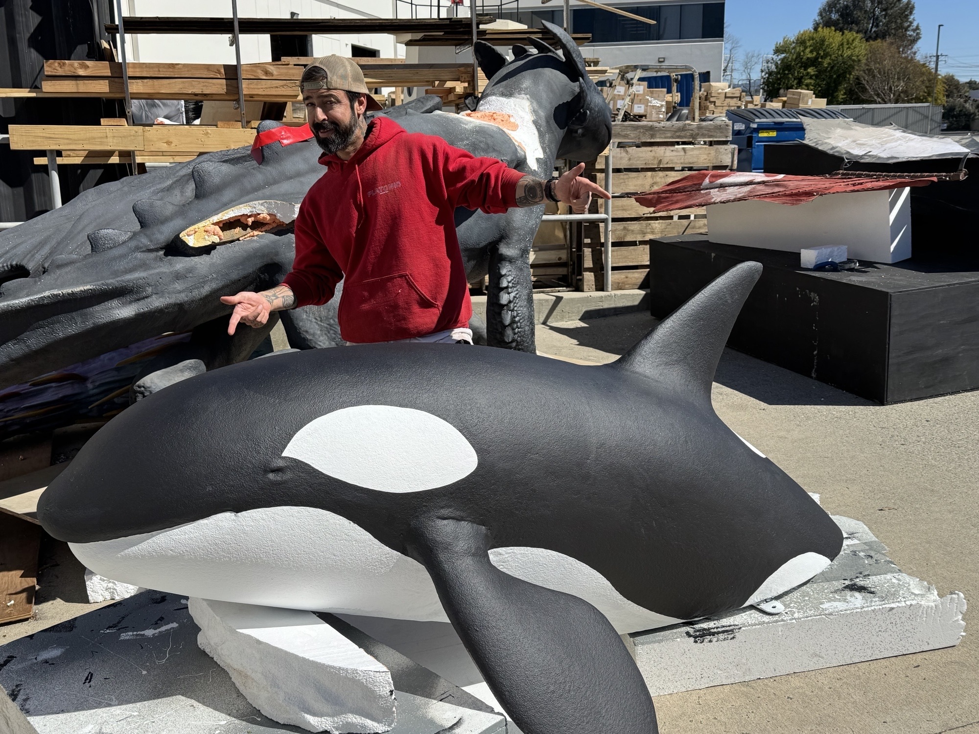 A man smiles and gestures toward a miniature orca whale sculpture soon to become part of the minigolf course