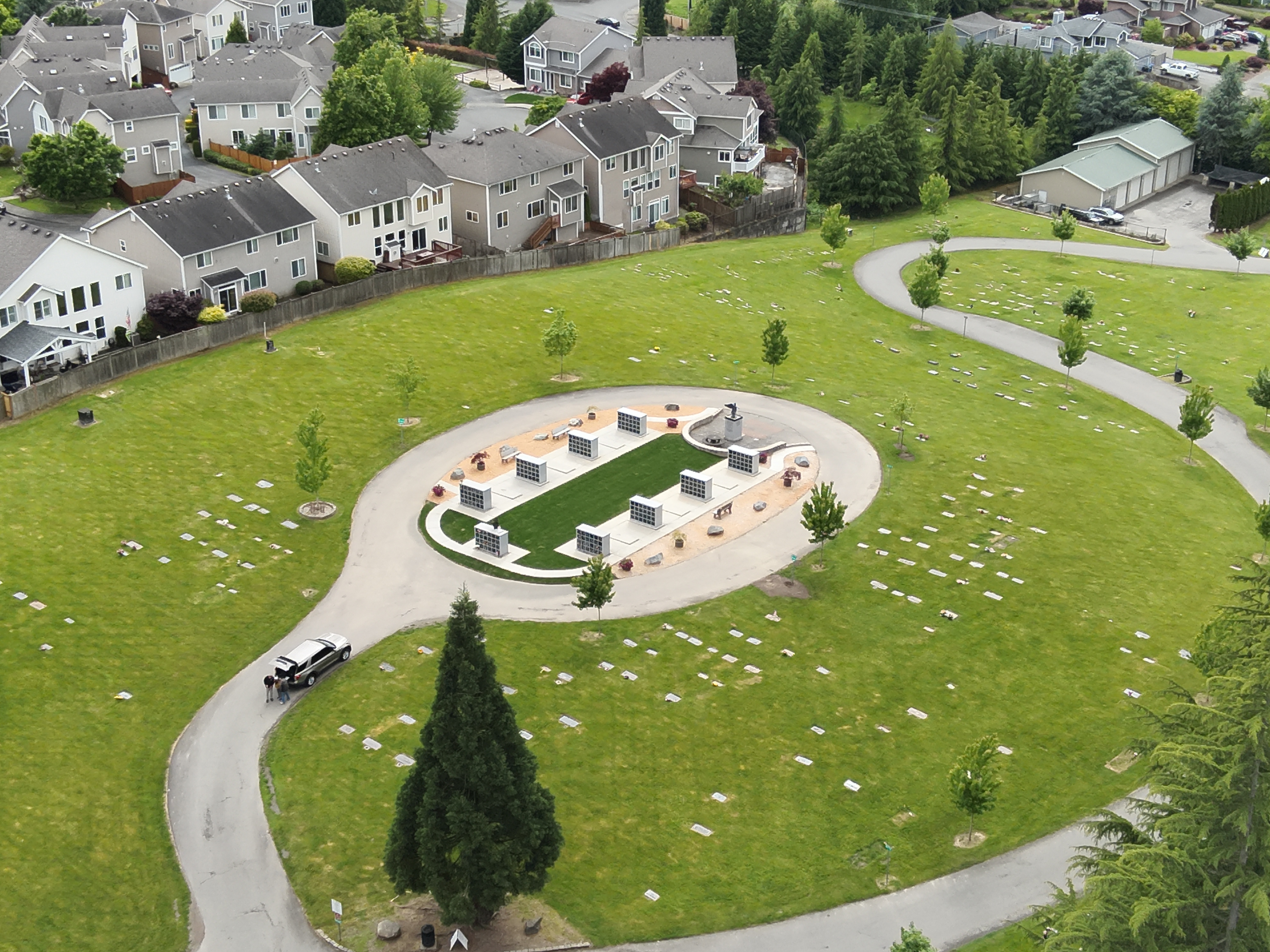 The columbarium is ringed by an asphalt drive and trees, surrounded by cemetary gravestones