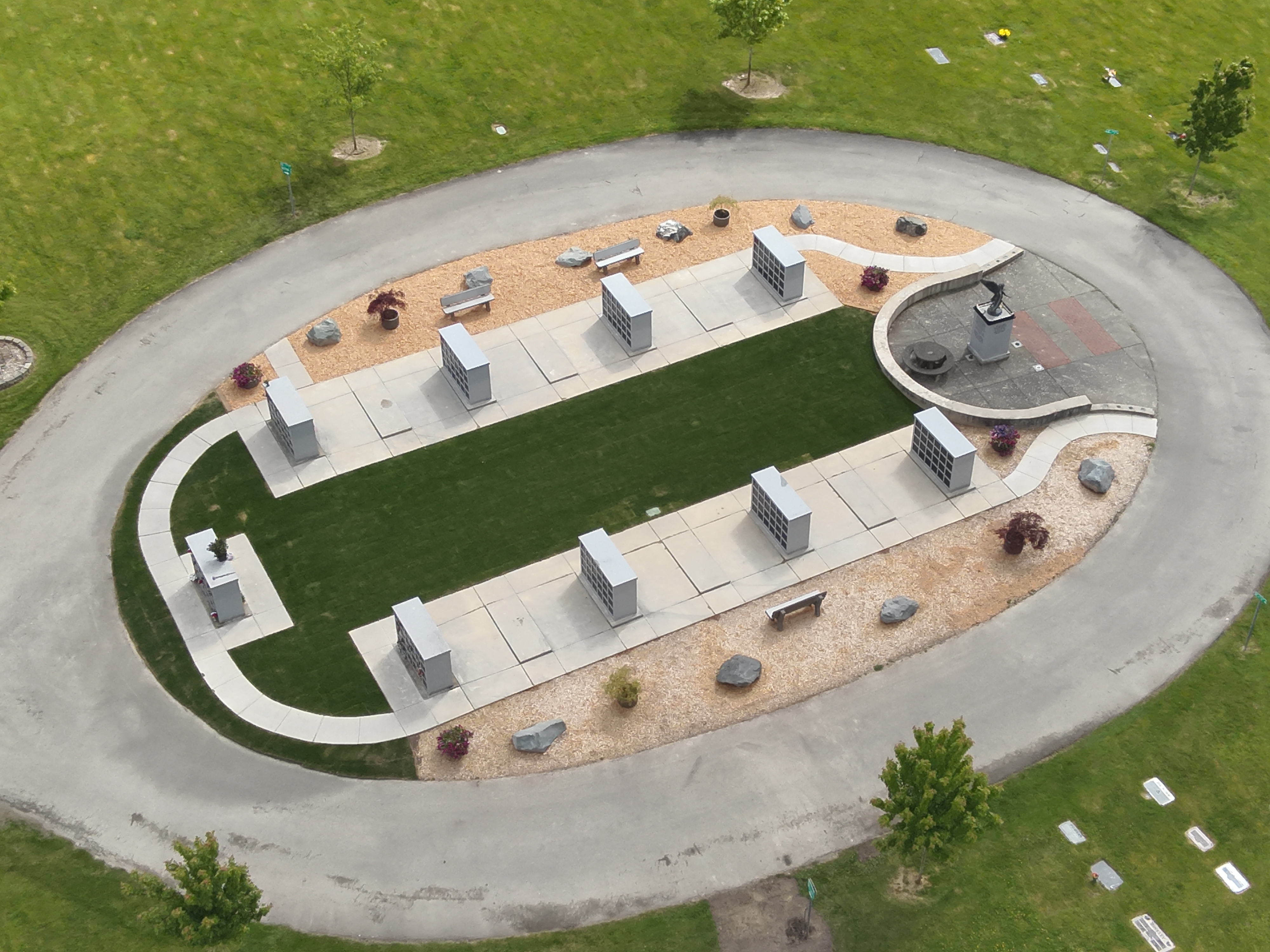 Eight crematory internments are laid out in two rows within an oval bordered by the driveway. One end of the columbarium is punctuated by a memorial statue and the ninth internment sits at the opposite end.