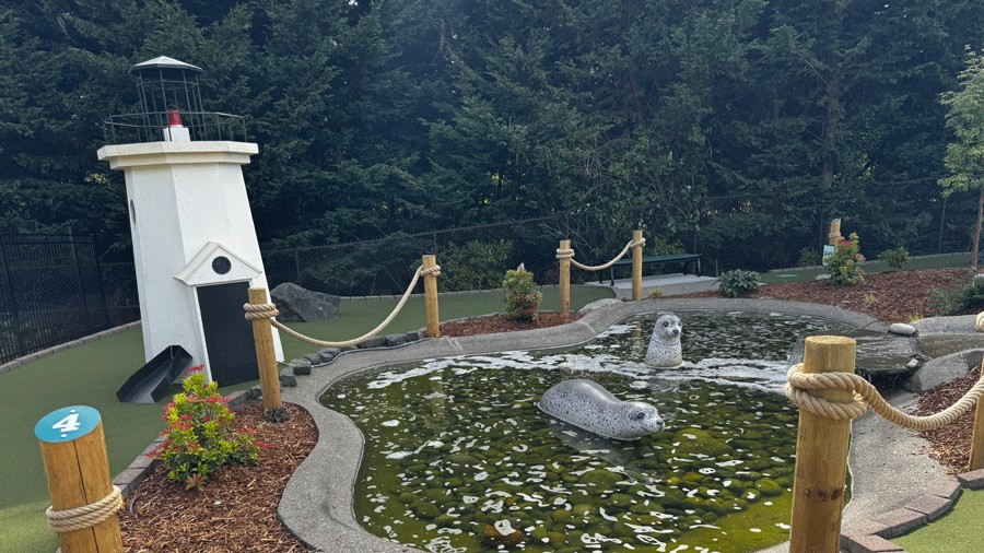 A miniature light house obstacle, marina-style post and rope barriers, and two seal statuettes in an organic-shaped pool characterize the fourth hole