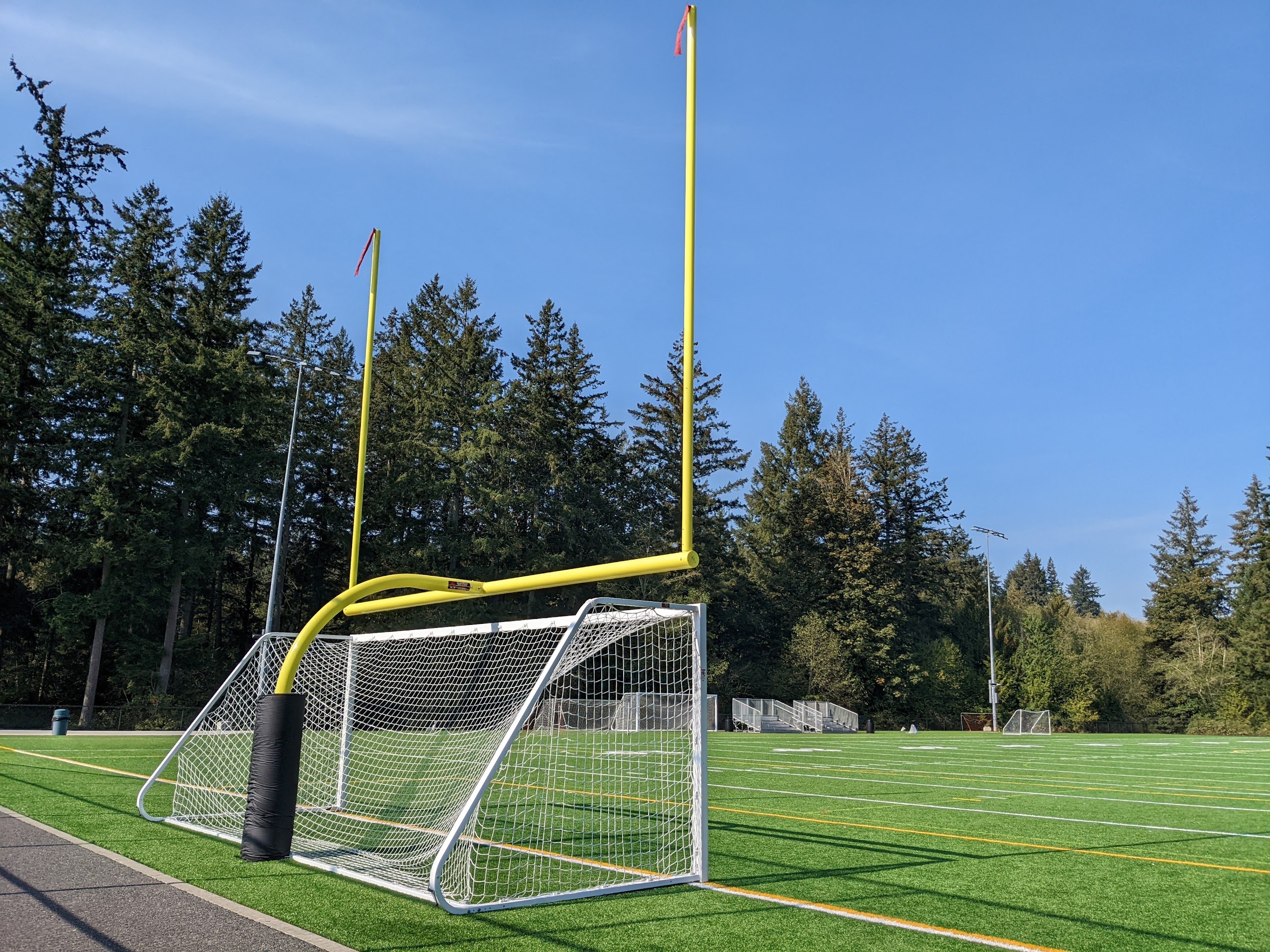 A white goalie net is stowed under a bright yellow field goal post at one end of the field